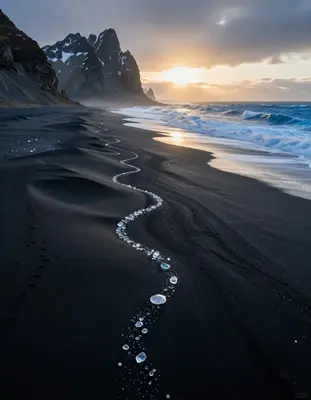 Aerial view of a surreal Icelandic black sand beach at golden hour, with undulating dunes of dark volcanic sand stretching to