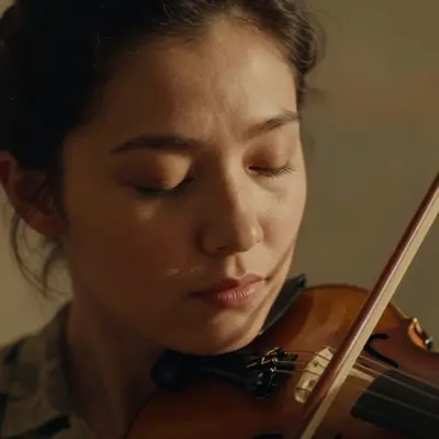 A close-up portrait of a violinist's face mid-bow-stroke, eyes closed in tender expression, with a warm golden hour rim light