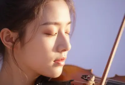 A close-up portrait of a violinist's face mid-bow-stroke, eyes closed in serene concentration, illuminated by a soft pastel g