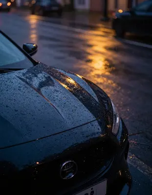 A dramatic still life photograph of rain on a sleek black sports car bonnet, captured with a Sony A7R IV and a 24mm f/1.4 len
