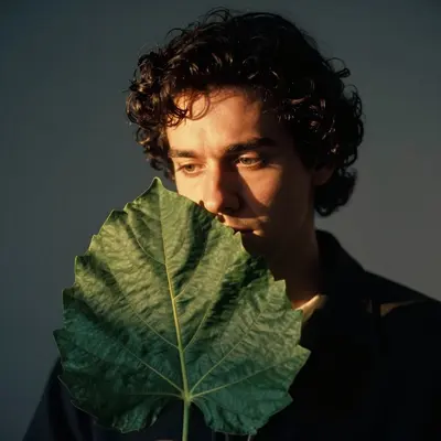 a head-and-shoulders portrait of a botanist with a large leaf held close to her face, illuminated by a soft, film noir-inspir