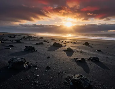 A high-contrast aerial view of a vast Icelandic black sand beach at golden hour, with dark volcanic rocks and jagged pebbles 