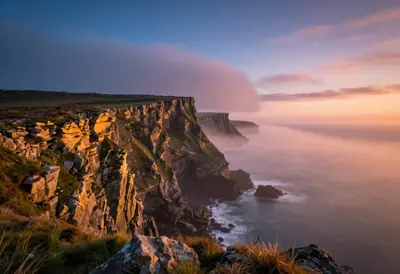 A hyper-detailed Cornish coastal cliff at dawn, with golden hour light casting a warm glow over the rugged, rocky shoreline, 