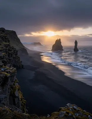 A serene Icelandic black sand beach at golden hour, with waves gently lapping at the shore, surrounded by rugged moss-covered